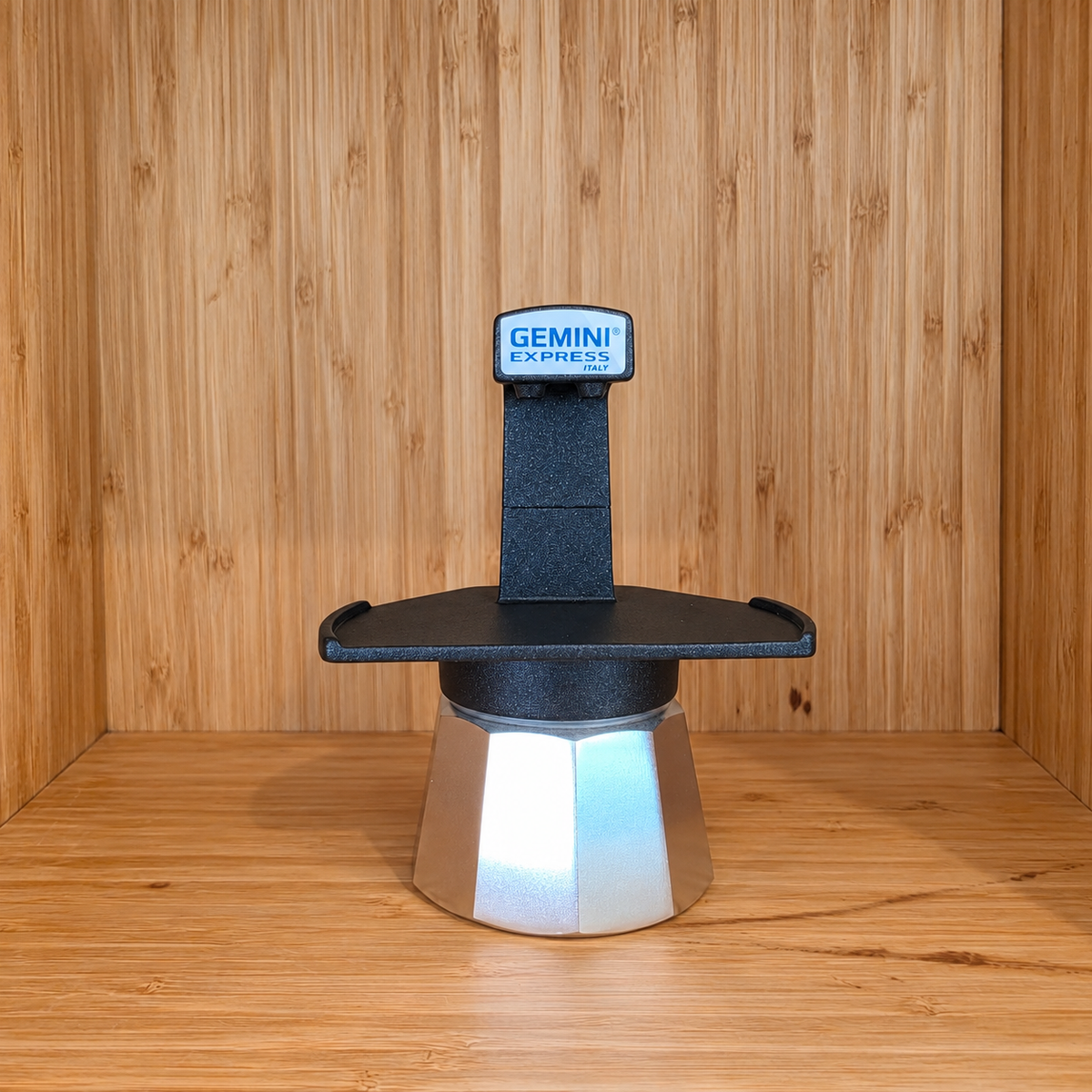 A Black Gemini Express moka pot centered against a wooden background.