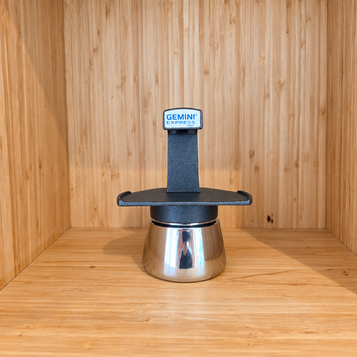 A Black Gemini Express moka pot centered against a wooden background.