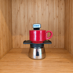 A Black Gemini Express moka pot centered with 1 red mug against a wooden background.