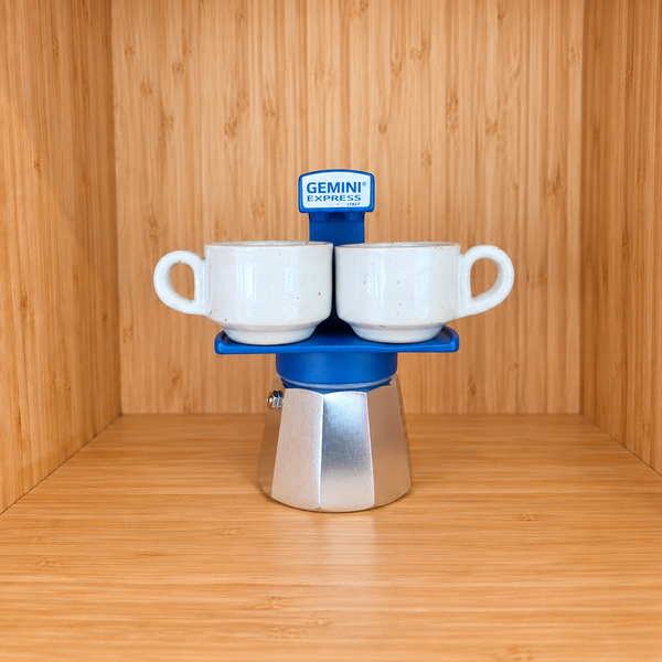 A blue Gemini Express Moka pot centered with 2 mugs on a light wood grain surface against a matching wood grain background.