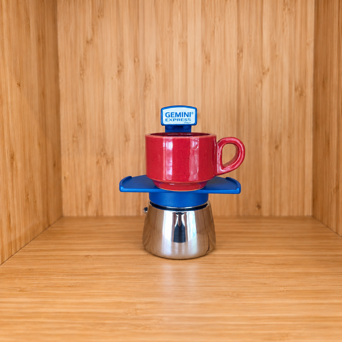 A blue Gemini Express Moka pot centered with 1 mug on a light wood grain surface against a matching wood grain background.