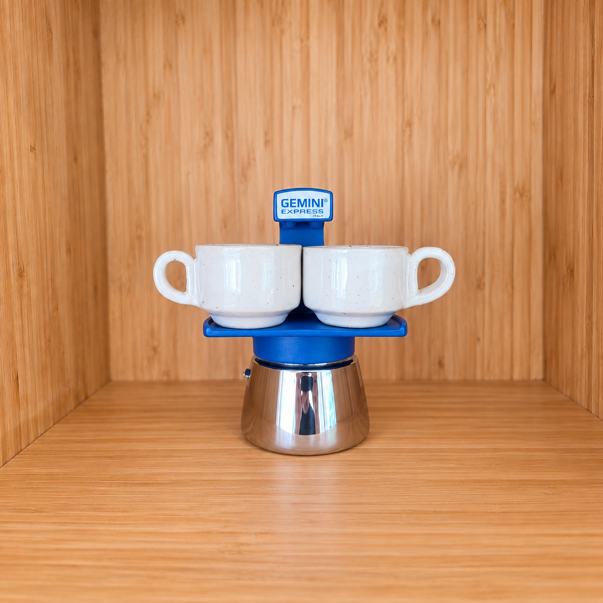 A blue Gemini Express Moka pot centered with 2 mugs on a light wood grain surface against a matching wood grain background.