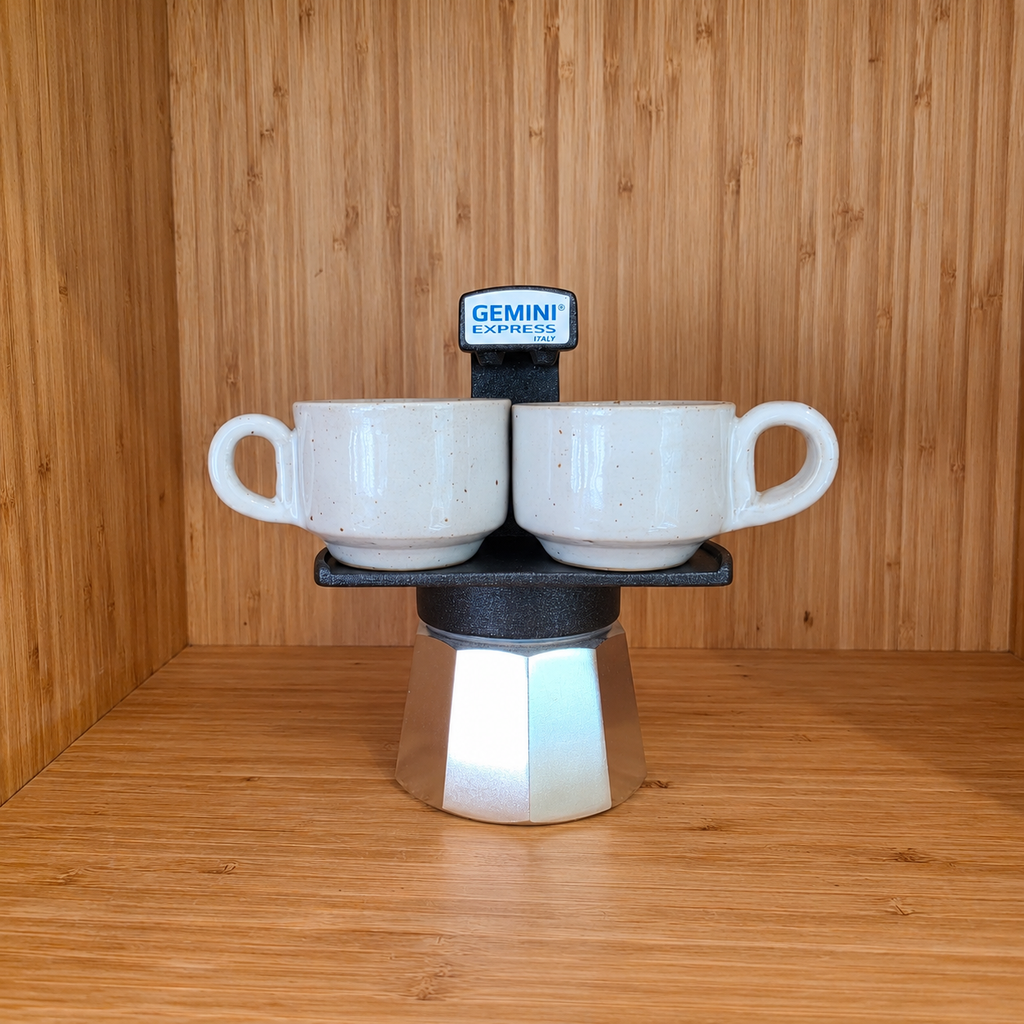 A Black Gemini Express moka pot centered with 2 mugs against a wooden background.