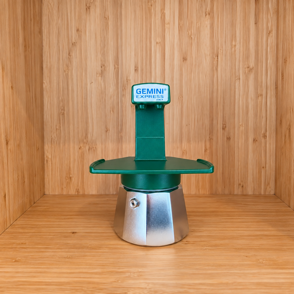 A green Gemini Express moka pot centered on a wooden surface against a wooden wall background.