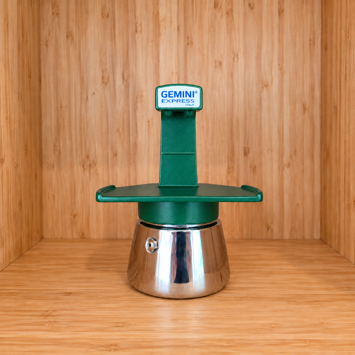 A Green Gemini Express espresso moka pot centered on a wooden surface against a wooden wall background.