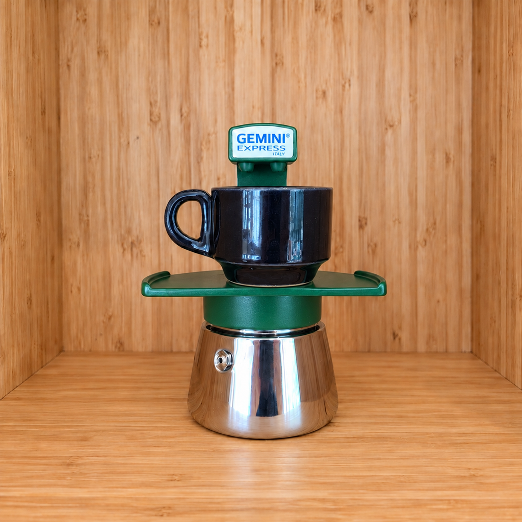 A Green Gemini Express espresso moka pot centered with 1 mug on a wooden surface against a wooden wall background.