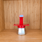 A red Gemini Espresso moka pot centered on a wooden shelf against a wooden wall.
