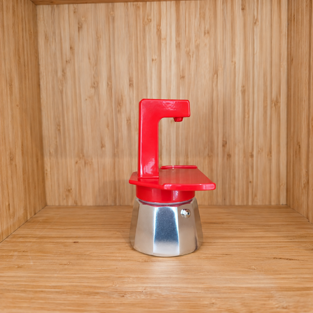 A red Gemini Espresso moka pot side view on a wooden shelf against a wooden wall.