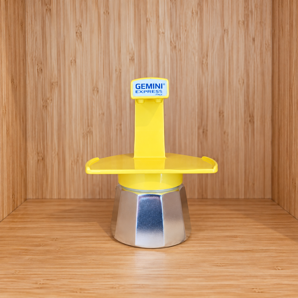 A Yellow Gemini Express espresso moka pot centered on a wooden surface against a wooden wall background.