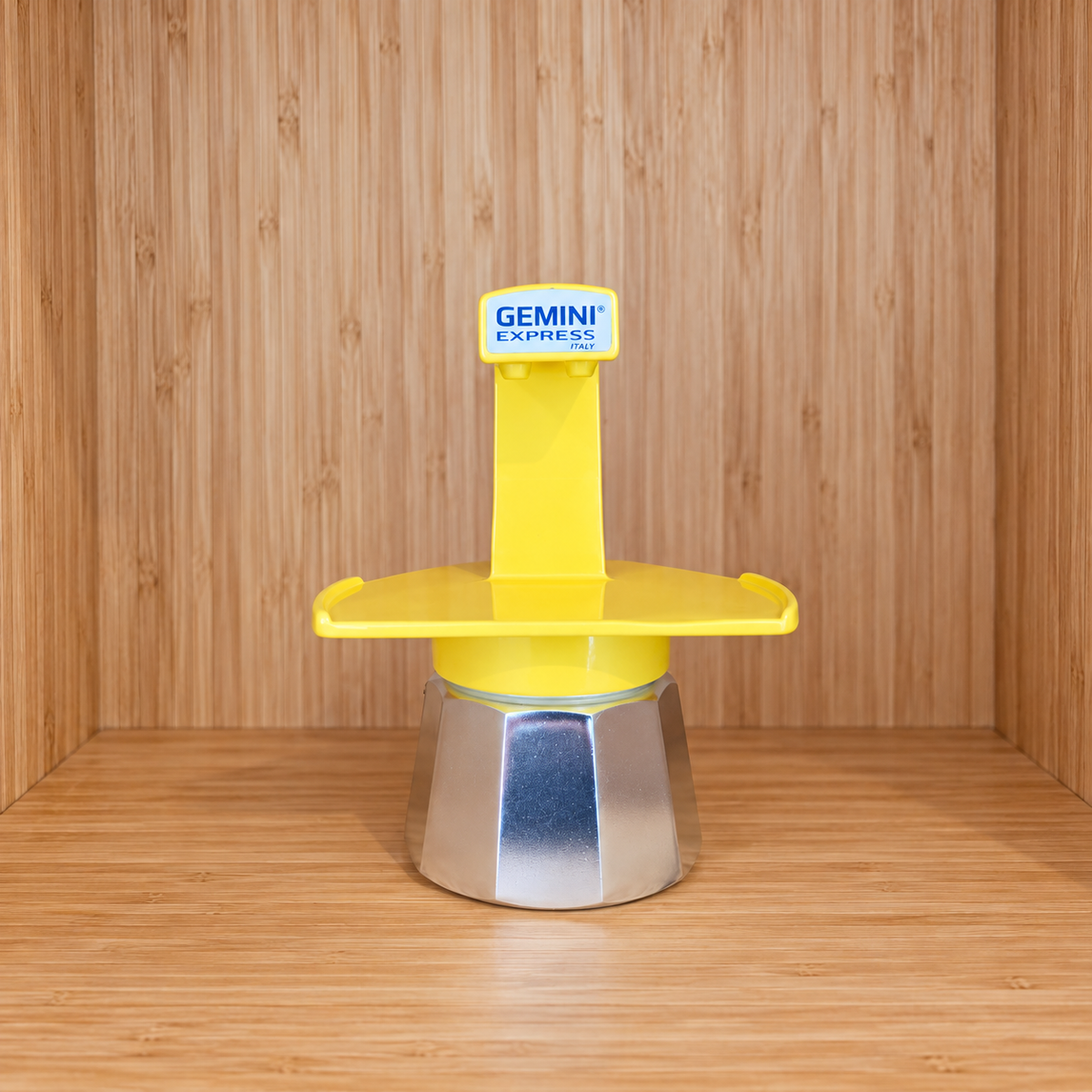 A Yellow Gemini Express espresso moka pot centered on a wooden surface against a wooden wall background.