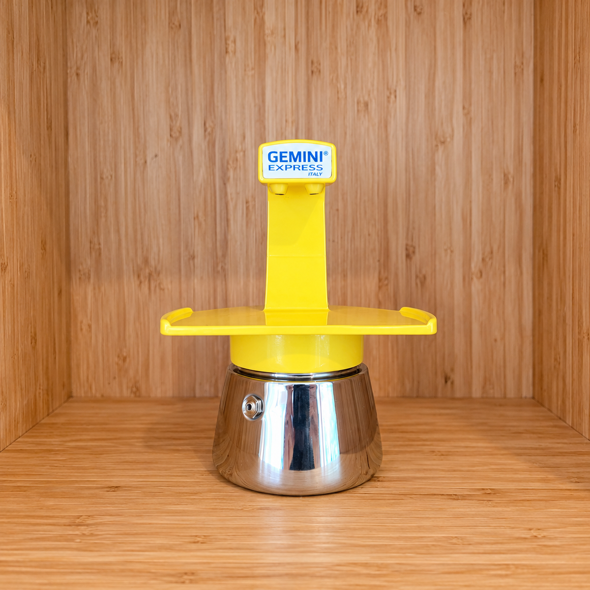 A yellow Gemini Express espresso moka pot centered on a wooden surface against a wooden wall background.