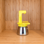 A yellow Gemini Express espresso moka pot side view on a wooden surface against a wooden wall background.