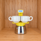 A yellow Gemini Express espresso moka pot centered with 2 mugs on a wooden surface against a wooden wall background.